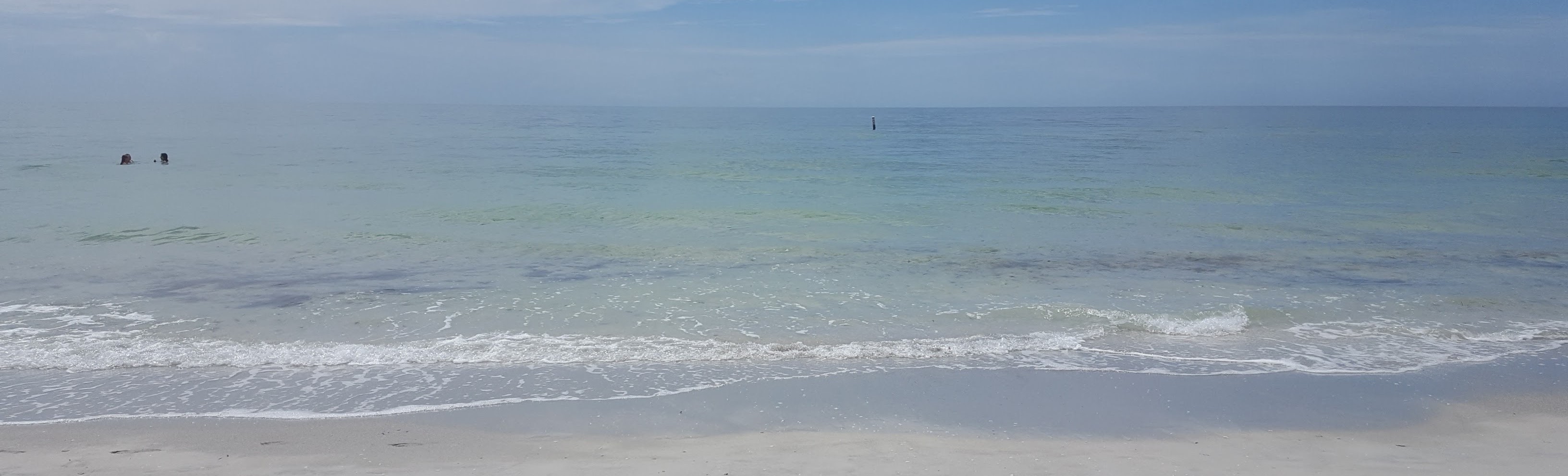 white sandy beach with turquoise water blending into horizon of blue sky and white clouds
